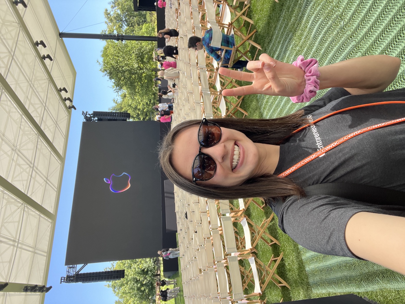 Lilly waving beside the WWDC24 sign on the lawn at Apple Park