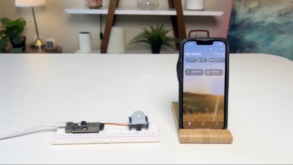 An ESP32 board with a motion sensor on a breadboard next to an iPhone showing the Apple Home app